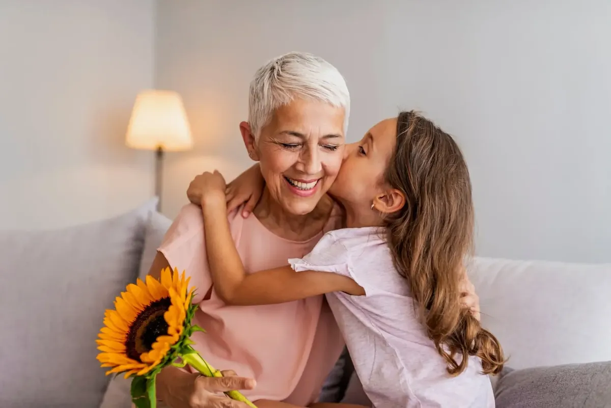 Grandmother smiling as her granddaughter kisses her cheek